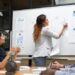 Team members discuss charts and plans around a whiteboard
